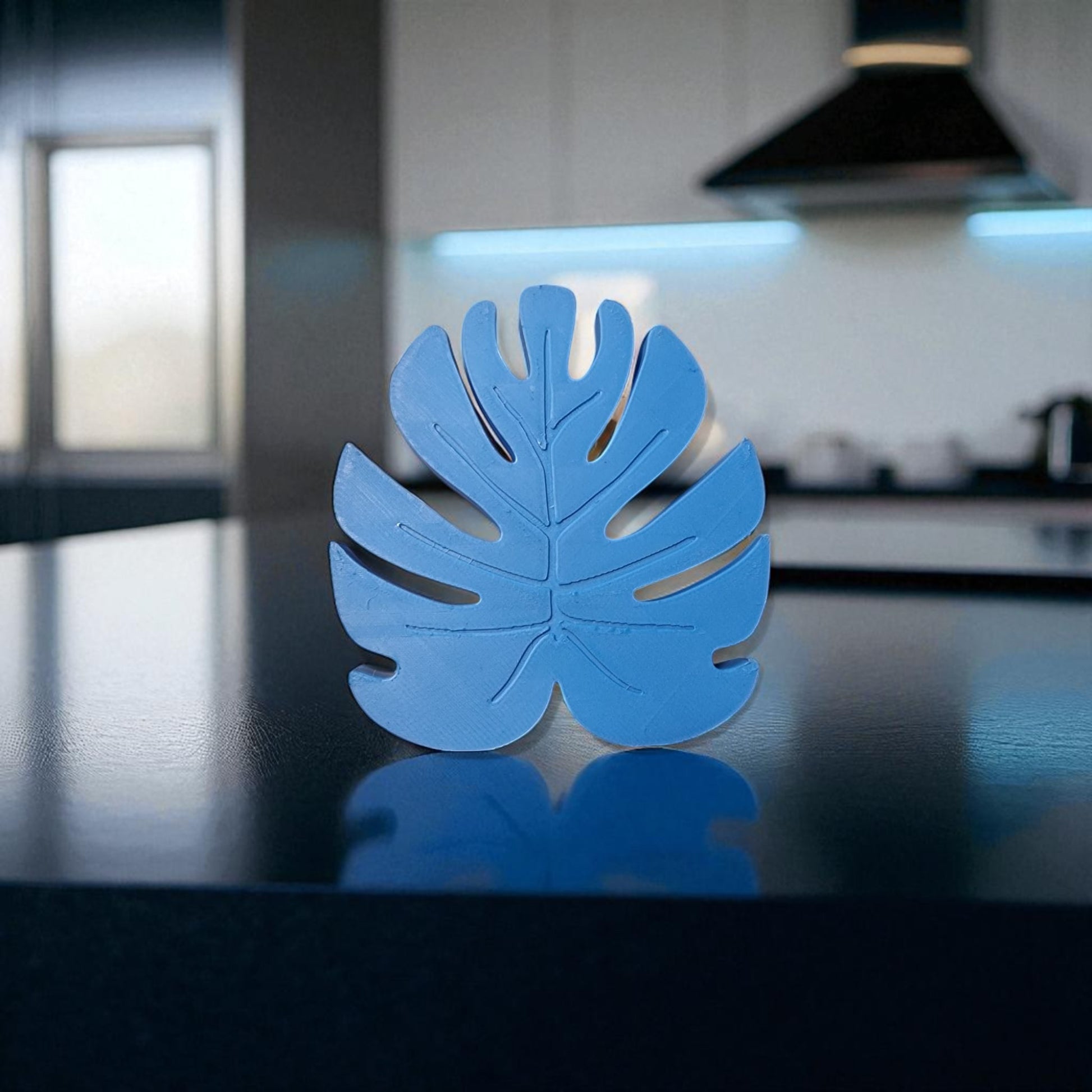 Blue leaf-shaped object on a reflective surface with a blurred kitchen background