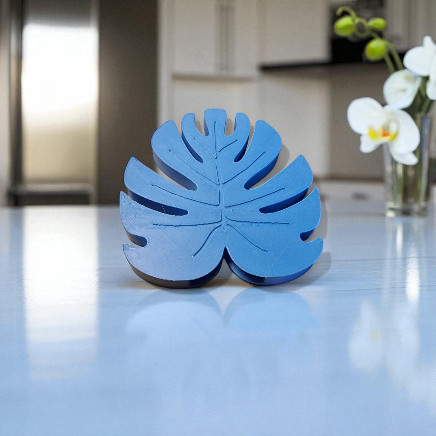 blue leaf-shaped object on a reflective surface with a kitchen background