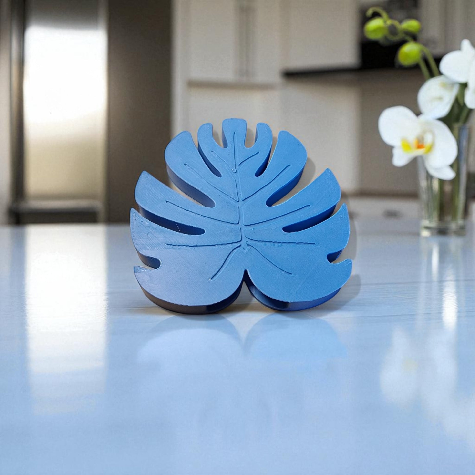 Blue leaf-shaped object on a reflective surface with a kitchen background